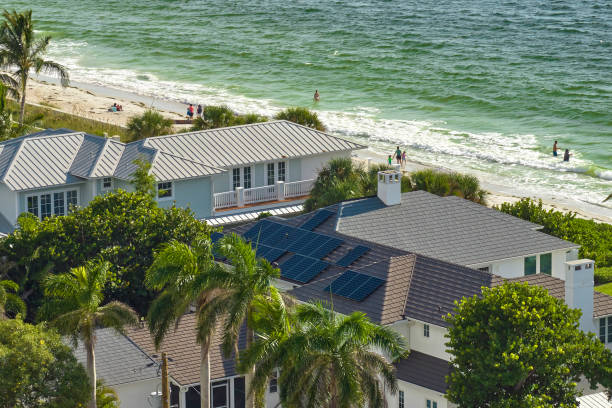 Aerial view of beachfront houses with solar panels on the roof, palm trees, and Miami homeowners walking along the shoreline, highlighting the work of a skilled roofer or contractor in this vibrant coastal community.
